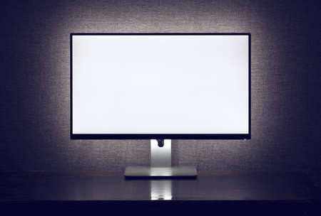 Blank monitor with backlight over gray wall in dark roomの写真素材