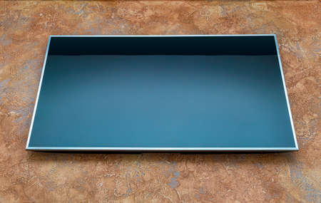 Big blank turned off lcd TV on orange wall, front bottom view
