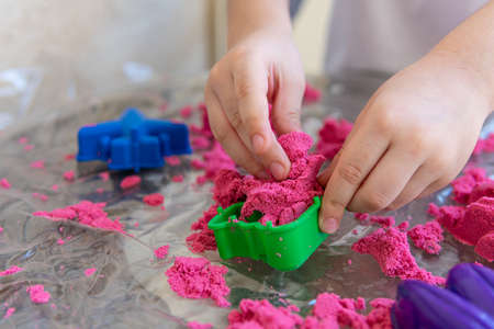 Closeup of childs hands playing in kinetic sand. Selective focus shot of kids hands with red kinetic sand and different color moldsの写真素材