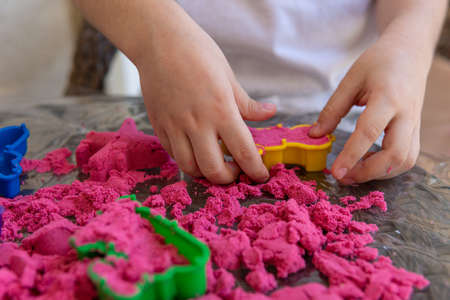 Closeup of childs hands playing in kinetic sand. Selective focus shot of kids hands with red kinetic sand and different color moldsの写真素材