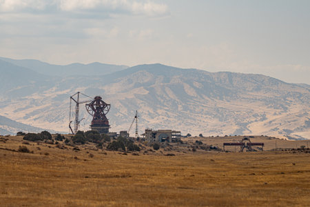 Abandoned and unfinished radio telescope complex standing on a dry plateau surrounded by mountains and grassland under clear skyの写真素材