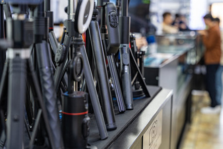 A close-up view of various photography accessories displayed in a store, including tripods and camera equipment, with customers in the background.の写真素材