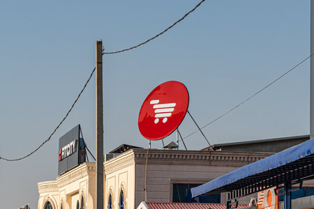 18 NOVEMBER, 2025 - Tashkent, Uzbekistan: vibrant red Korzinka logo is prominently displayed atop a building, contrasting with the clear blue skyのeditorial素材