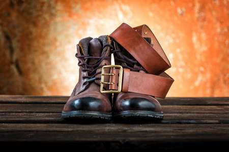 Men's winter boots of brown colour and leather belt with buckle isolated on rusty wooden background.