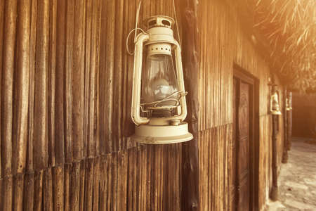 Old fashioned vintage kerosene oil lantern lamp with aged wooden wall and weathered grass roof.の写真素材
