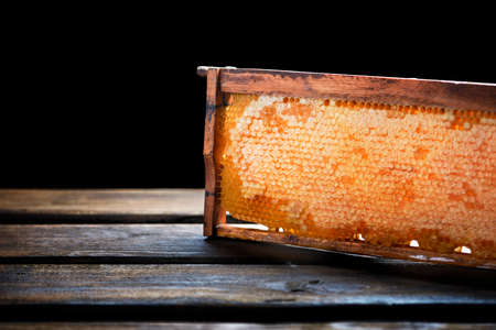 Wooden frame with honeycomb full of honey, on wooden pallet, isolated on blackの写真素材