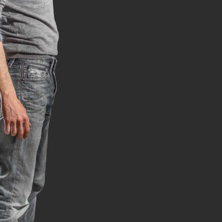 Young fashion man's legs in jeans and grey pullover on black background