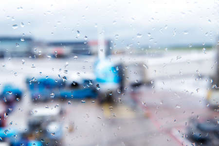 Abstract defocused bokeh of airplane at airport gate with sun coming out after the rain. Modern travel concept and wander lifestyle at sunset. Focus on raindrops with warm vintage filtered lookの写真素材
