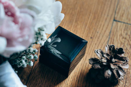 Bridal bouquet of roses, wedding rings in the box and pine cone on a wooden planks
