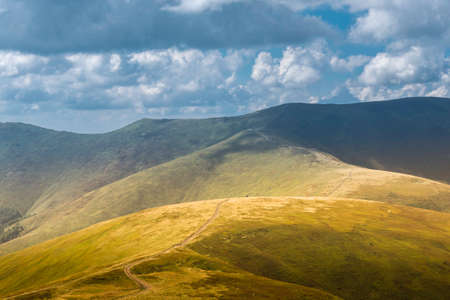 Summer view of Carpathian Mountains and Valleys, under blue sky with clouds. Mountain road goes on top of the hills on sunset landscape.の写真素材