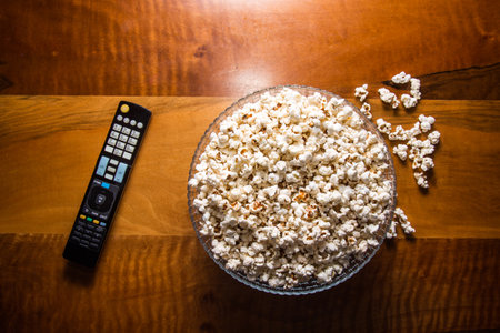 Tv remote control and popcorn on a wooden brown coffee table. Concept of stay home in the pandemic.