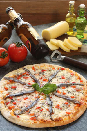 Anchovies pizza with a bottle of beer and ingredientsの写真素材