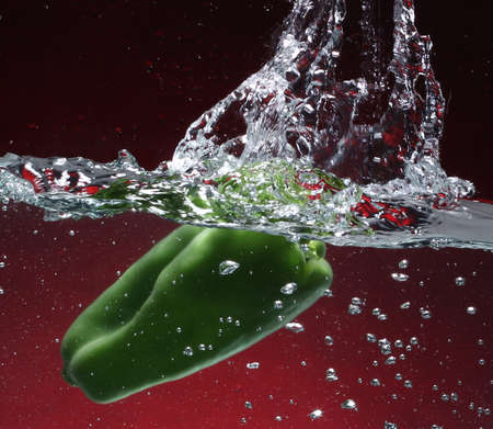 Green pepper falling into water  Red background