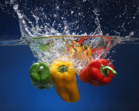 Three peppers falling into water  Blue background
