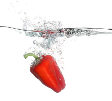 Red pepper falling into water over white backgroundの写真素材