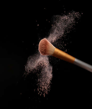 Make up brush with cosmetic powder splash, over black background. splash image
