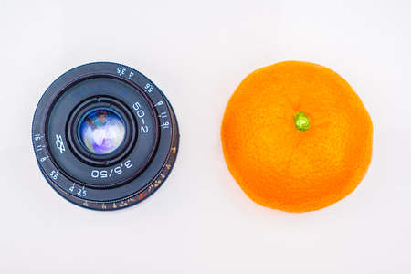 Old lens and tangerine or orange on white table background, top view