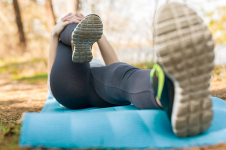 Girl in a sport suit, outdoors, kneading her legs on a blue sports mat