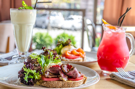 A sandwich with ham cheese and herbs on a white plate, on a wooden table, a cocktail and juiceの写真素材