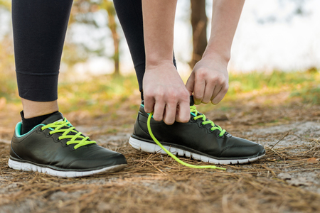 A girl in sports pants and a hoodie, standing tied up her shoelaces on sports shoesの写真素材