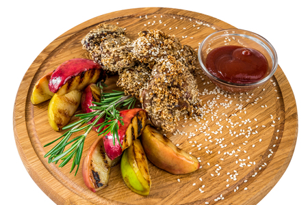 Fried meat with sesame, apples and sauce on a wooden boardの写真素材