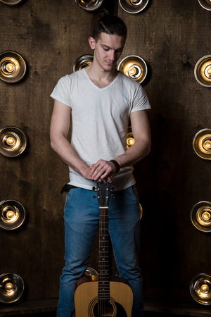 Guitarist, music. A young man stands with an acoustic guitar in the background with the lights behind himの写真素材