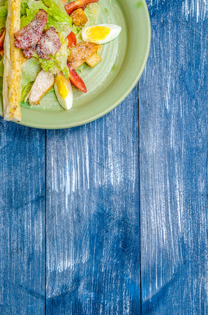 Corner salad of eggs, tomatoes, lettuce, with bread on a green plate, stand on a blue denim backgroundの写真素材