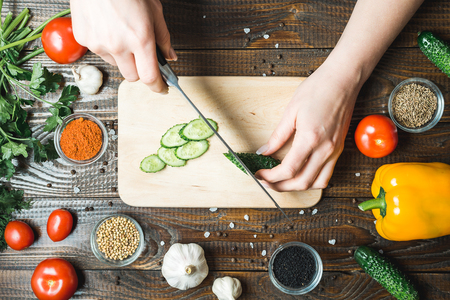 women's hands cut a cucumber, close to the tomatoes, paprika and garlicの写真素材