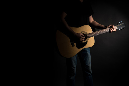 The guitarist in jeans plays an acoustic guitar, on the right side of the frame, on a black backgroundの写真素材