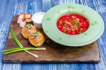 Red soup in a green plate, rolls, bacon, onions and sauce on a wooden board stand on a blue denim backgroundの写真素材