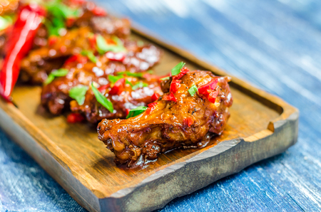 Hot meat dish - Fried chicken legs with curry sauce and red pepper on a wooden boardの写真素材