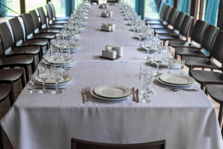 Interior of the restaurant, cafe. Tables with utensils, plates, wiches, knives, glasses and wine glasses, and brown chairs, preparation for celebrationの写真素材