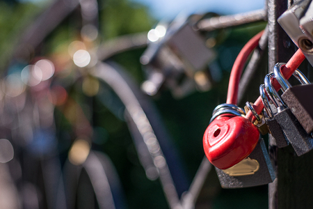 The lock is red in the form of a heart, hanging next to other locksの写真素材