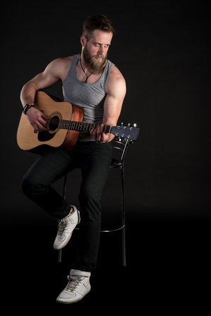 A charismatic man with a beard, playing an acoustic guitar, on a black isolated backgroundの写真素材