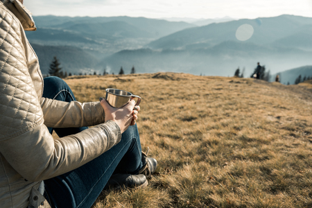 girl with a metal cup sits on a background of mountainsの写真素材