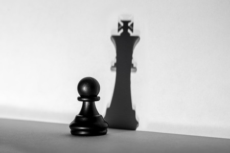 Chess pawn standing in a spotlight that make a shadow of king with darkness artistic conversion. Horizontal frameの写真素材