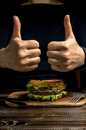 Healthy lifestyle, proper nutrition. Female hands show "coolly" over a healthy rice burger with vegetables, herbs and cutlet on a wooden board. Vertical frameの写真素材