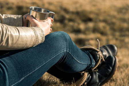 girl with a metal cup sits on a background of mountainsの写真素材