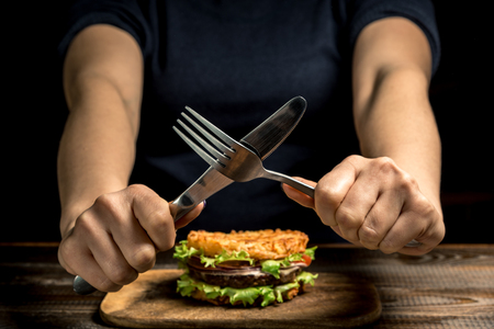 Healthy lifestyle, proper nutrition. Female hands show ban on wholesome rice burger with vegetables, herbs and cutlet on a wooden board. Horizontal frameの写真素材