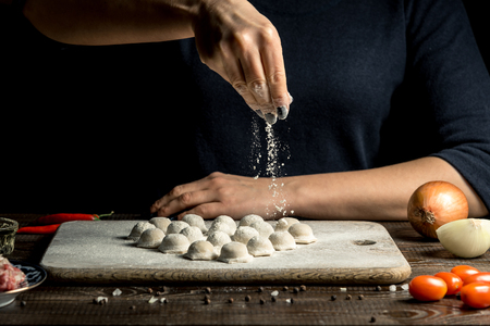 Uzbek national food Chuchvara, like dumplings, lie in the shape of a heart, on a wooden board, hands are crushing flour from above. Horizontal frameの写真素材