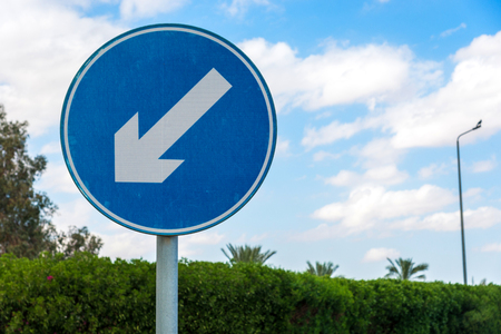 Round blue road sign with white diagonal warning arrowの写真素材