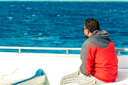 the guy in the jacket sits on a white yacht and looks at the seaの写真素材