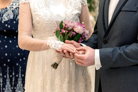 The moment of the exchange of the rings of the newlyweds, the bridegroom puts the ring on the bride. Horizontal frameの写真素材