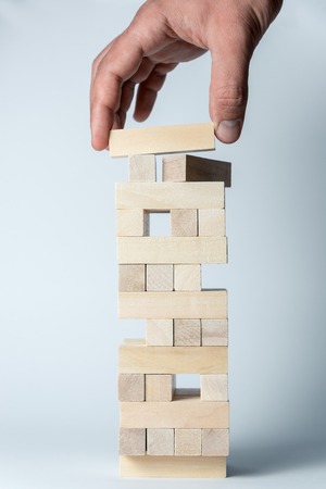 Male hand puts a cube on the tower of wooden cubes, as a symbol of support, teamwork and business developmentの写真素材