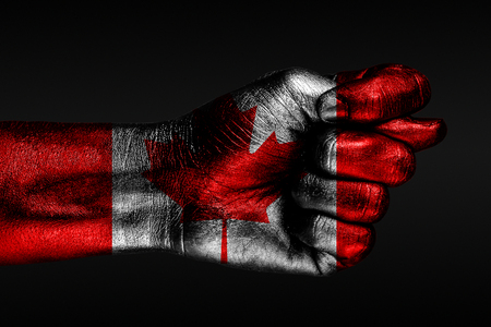 A hand with a painted Canada flag shows a fig, a sign of aggression, disagreement, a dispute on a dark background. Horizontal frameの写真素材