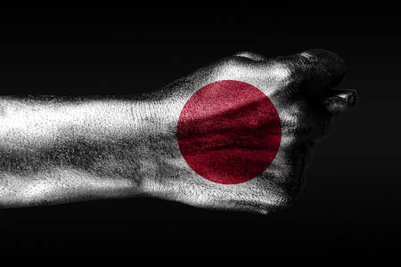 A hand with a painted Japan flag shows a fig, a sign of aggression, disagreement, a dispute on a dark background. Horizontal frameの写真素材