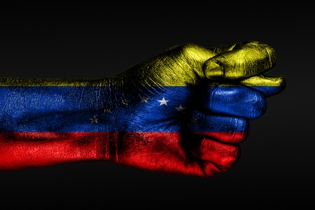 A hand with a painted Venezuela flag shows a fig, a sign of aggression, disagreement, a dispute on a dark background. Horizontal frameの写真素材