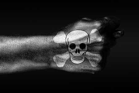 On a hand with a painted human skull and bones depicted a fig, a sign of aggression, disagreement, piracy, on a dark background. Horizontal frameの写真素材
