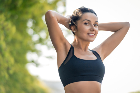 Slim beautiful girl with dark hair in a sports uniform is stretched in nature with a smile and look into the frame, a symbol of a healthy lifestyle and athletic body. Horizontal frameの写真素材