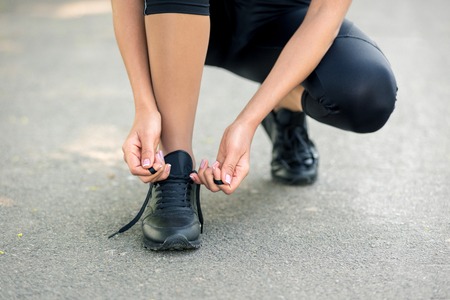Women's hands lace up black sneakers, a symbol of preparation for running or sports. Horizontal frameの写真素材